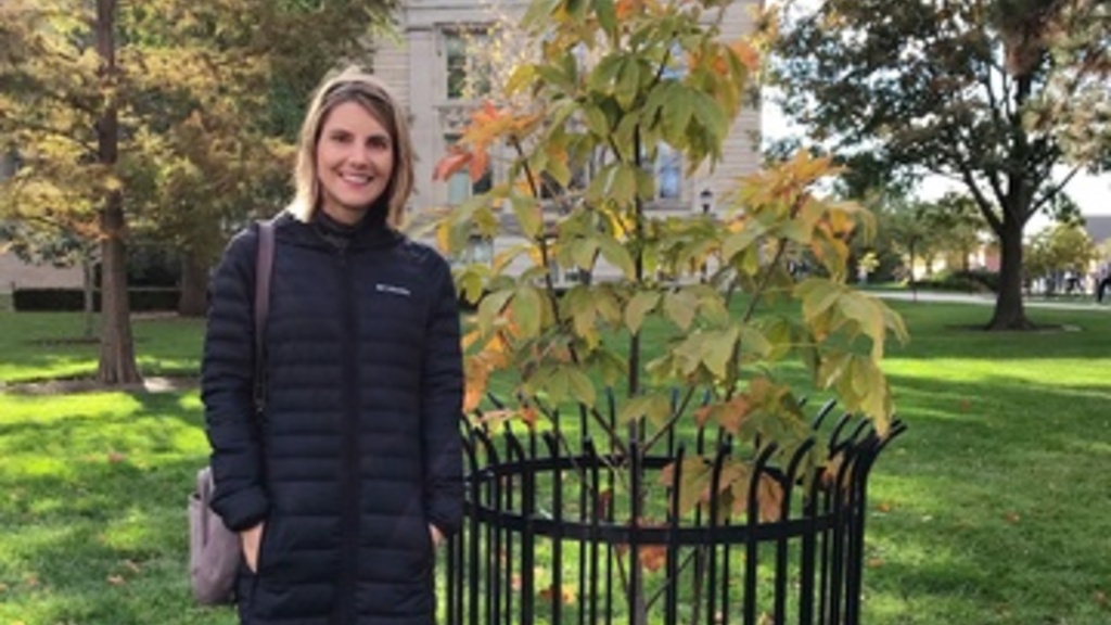 Kirsten Kumpf Baele standing next to the Anne Frank sapling on the UI campus